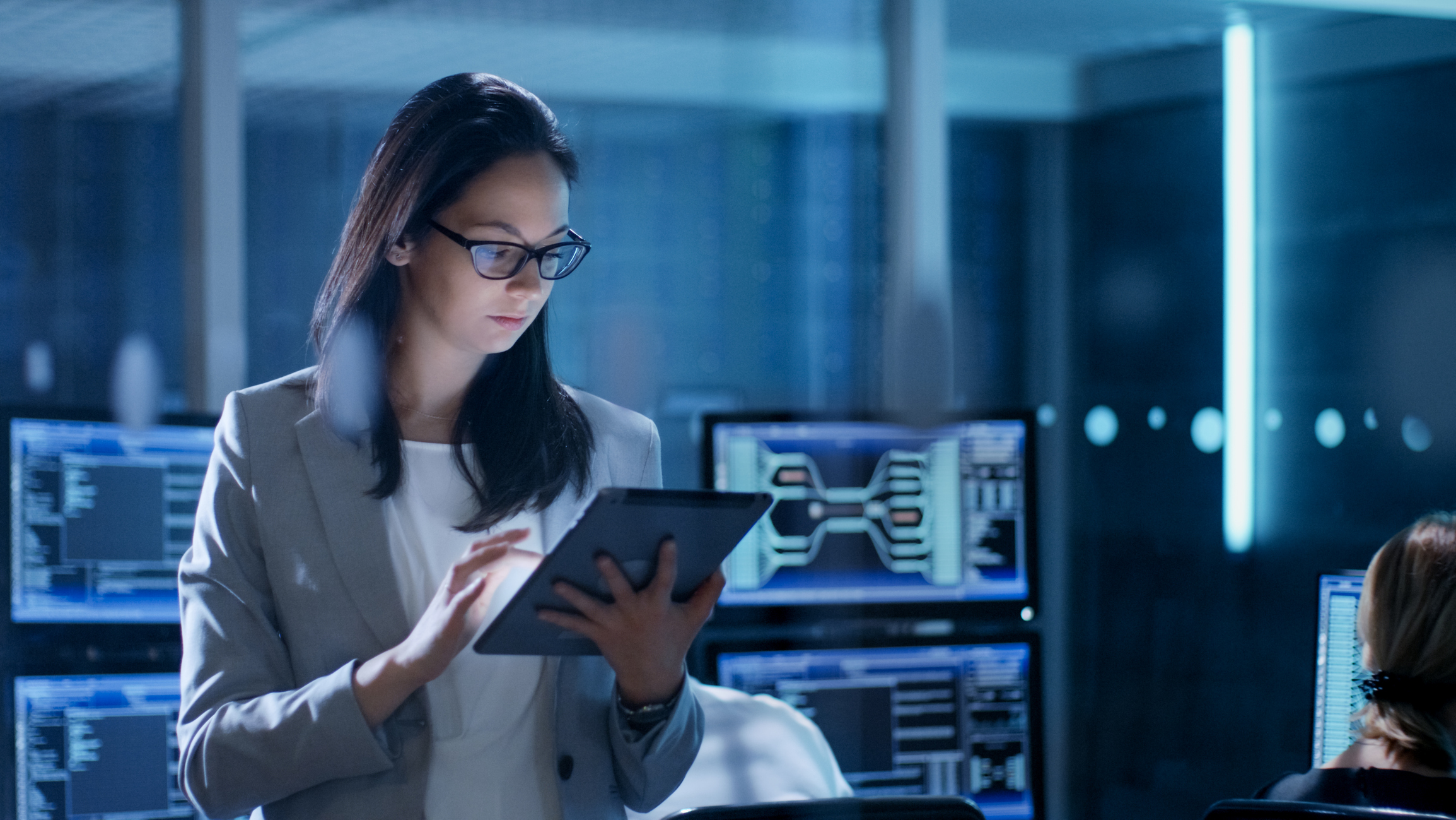 Female in a darkened server room checking data on a tablet device.